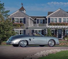 an old silver sports car parked in front of a large house with flowers on the windows