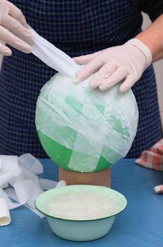 a person in white gloves is making a vase with green and white paint on it