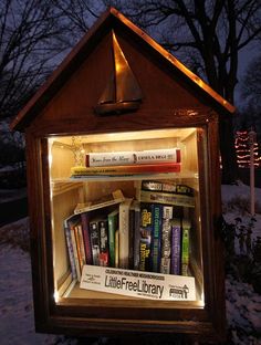 a lit up book shelf with books in it and snow on the ground behind it