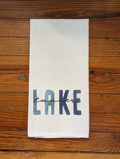 a white tea towel with the word lake printed on it, sitting on a wooden floor