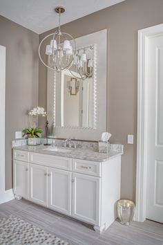 a white bathroom with a chandelier and marble counter top, along with a large mirror on the wall