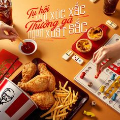 a table topped with fried chicken and french fries next to cups of soda, dices and chips