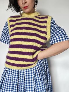 a woman wearing a yellow and purple striped sweater with her hands on her hips, leaning against a wall