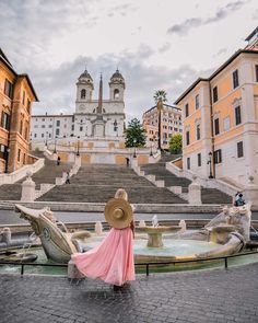 a woman in a pink dress and straw hat is standing on the steps leading to a fountain