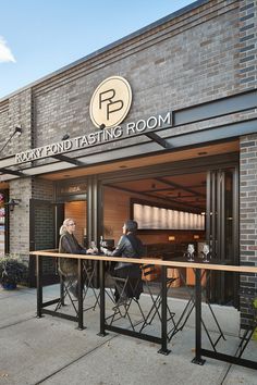 two people sitting at tables in front of a brick building with the words army fond tasting room on it