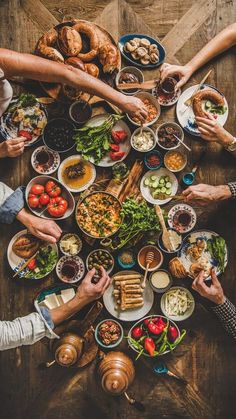 several people sitting around a table full of food and drinks, all holding their hands together