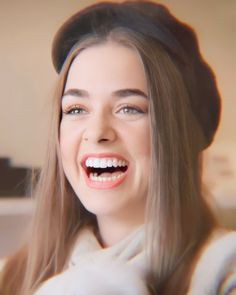 a woman with long brown hair is smiling and wearing a black hat on her head