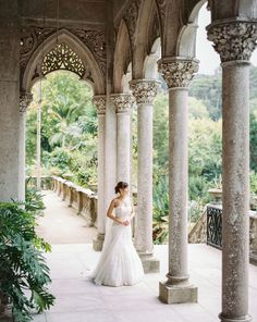 a woman in a wedding dress is standing under an ornate building with columns and arches