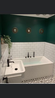 a bath tub sitting next to a sink in a room with green walls and black and white flooring