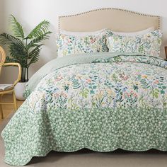 a bed with green and white floral bedspread on top of it next to a chair