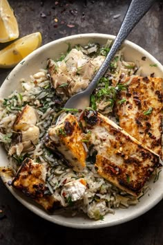 a white bowl filled with rice and chicken on top of a table next to lemon wedges