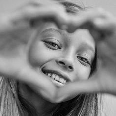 a girl making a heart with her hands and smiling at the camera, black and white photograph