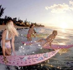 three girls on surfboards in the ocean with sun shining behind them and water splashing around them