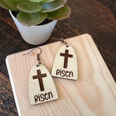 two wooden earrings with crosses on them sitting next to a potted succulent plant