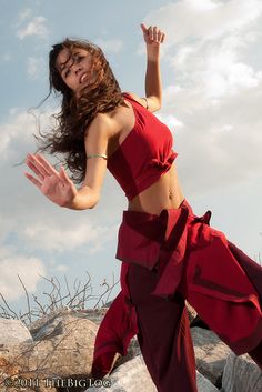 a woman in a red dress is dancing on rocks