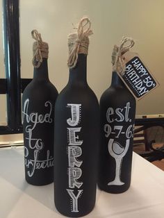 three black wine bottles with white writing on them sitting on a table in front of a mirror