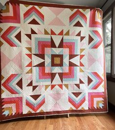 a large quilt hanging from the ceiling in a room with wooden floors and windows,