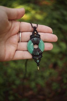 a hand holding a green beaded necklace with an oval pendant on it's end