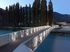 a bridge over a body of water with trees on both sides and mountains in the background