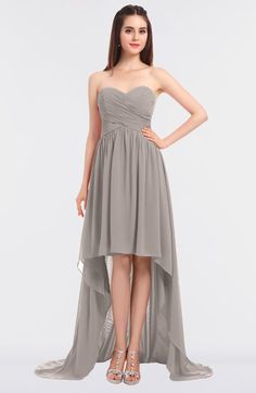 a woman wearing a strapless grey dress with high low slits and an asymmetric