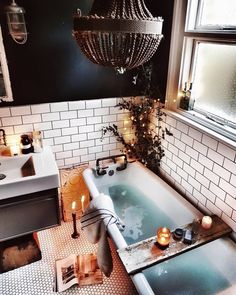 a bath tub sitting next to a window in a bathroom under a chandelier