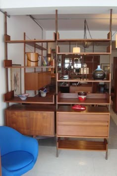 a blue chair sitting in front of a wooden shelf filled with shelves and bowls on top of it