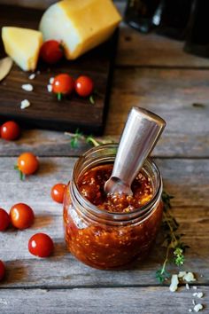 a glass jar filled with tomato sauce next to cheese and tomatoes on a wooden table