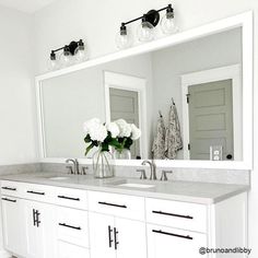 a white bathroom with double sinks and large mirrors on the wall above them is decorated with flowers