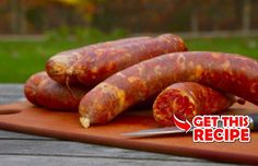 three sausages are on a cutting board with a knife next to it and some grass in the background