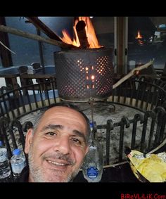 a man sitting in front of a fire pit with water bottles on the table next to him