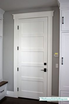 a white door in the corner of a room with gray walls and wood flooring