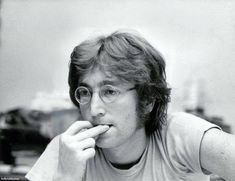 a man in glasses is eating something with his hand and looking at the camera while sitting down