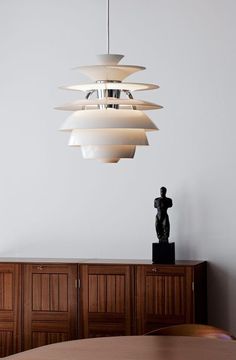 a modern light fixture hanging from the ceiling above a table with a statue on it