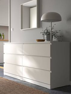 a white dresser sitting next to a lamp on top of a wooden floor