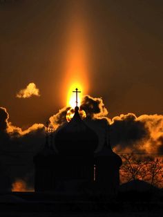 the sun is setting over a church with clouds in the background and a cross on top