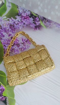 a gold purse sitting on top of a white table next to purple lilacs and green leaves