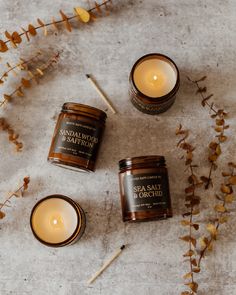 three candles sitting on top of a table next to some dried flowers and plants with one candle lit