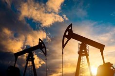 oil pumps silhouetted against the setting sun with clouds in the background and blue sky