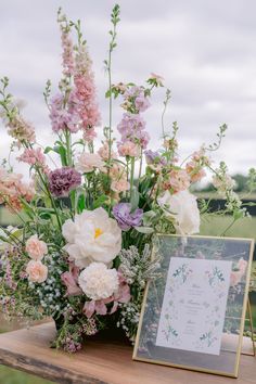 an arrangement of flowers in a vase on a table with a card and photo frame