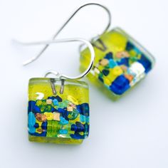 a pair of earrings with green and blue designs on them, hanging from silver earwires