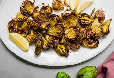 a white plate topped with brussel sprouts next to lemon wedges