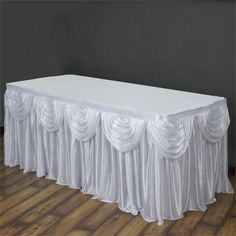 a white table with pleated drapes on the top and bottom, in front of a gray wall