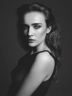 a black and white photo of a woman with her hair in a pony tail, looking at the camera