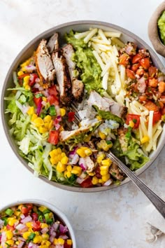 two bowls filled with different types of food and one bowl has chicken, lettuce, tomatoes, corn, and other vegetables