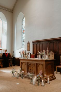 flowers and candles are placed on the floor in front of an old church pew with stained glass windows