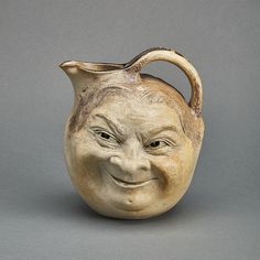 a ceramic jug with a smiling face on it's front and back sides, against a gray background