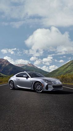 a silver sports car parked on the side of a road in front of some mountains