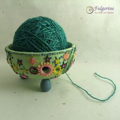 a green ball of yarn sitting in a bowl on top of a wooden stand next to a string