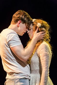 a man and woman standing next to each other in front of a dark background with their arms around each other