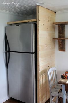 a kitchen with a refrigerator, table and chair next to the wall that is made out of wood